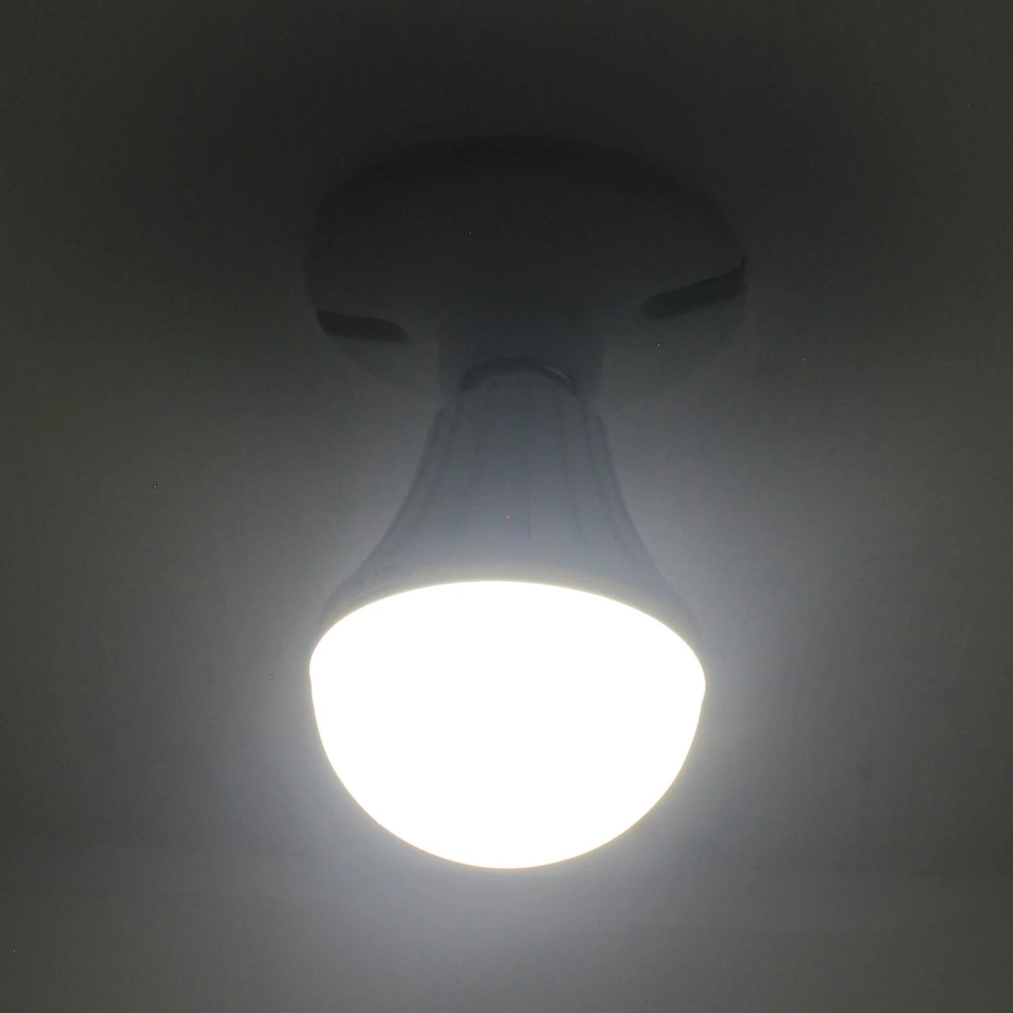 Bombilla LED tipo bulbo encendida con luz blanca brillante, vista desde abajo en un techo oscuro